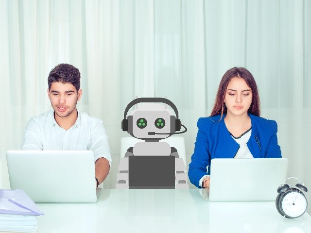 Working robot between a man and a woman in office working on computers. 