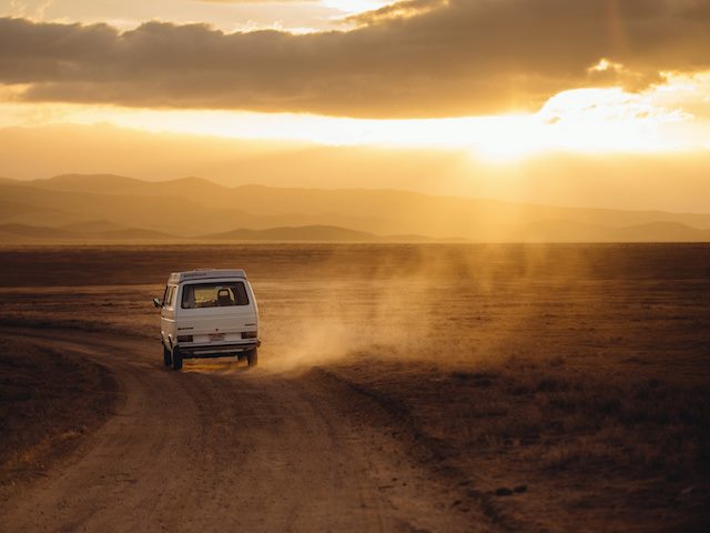 a van driving into the sunset with clouds over the sun