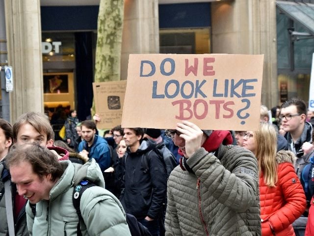 People walking and a man holding a sign that says, "Do we look like bots?"
