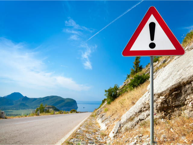 Warning road sign with an exclamation mark in red triangle on mountain highway
