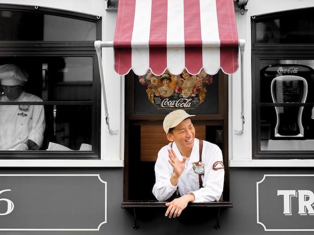 smiling employee waving from window of a restaurant (food truck?) 