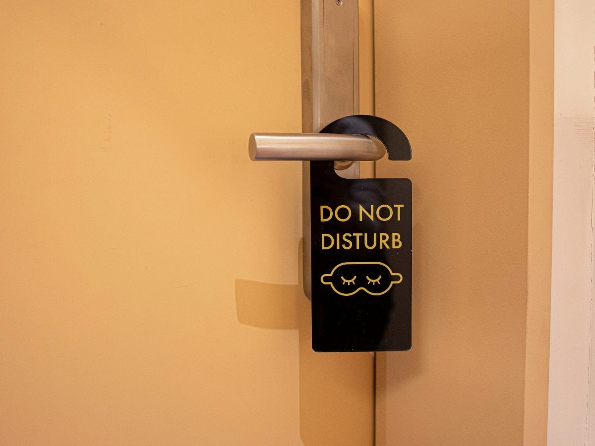 Black “Do Not Disturb” door hanger with a sleeping face icon hanging from a hotel room door handle against a beige door.