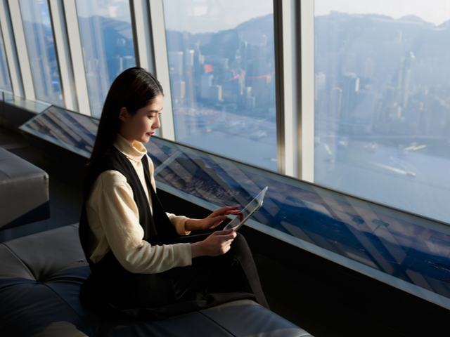 A businesswoman working remotely via her tablet. Sitting at a window - Unified Communications Concept