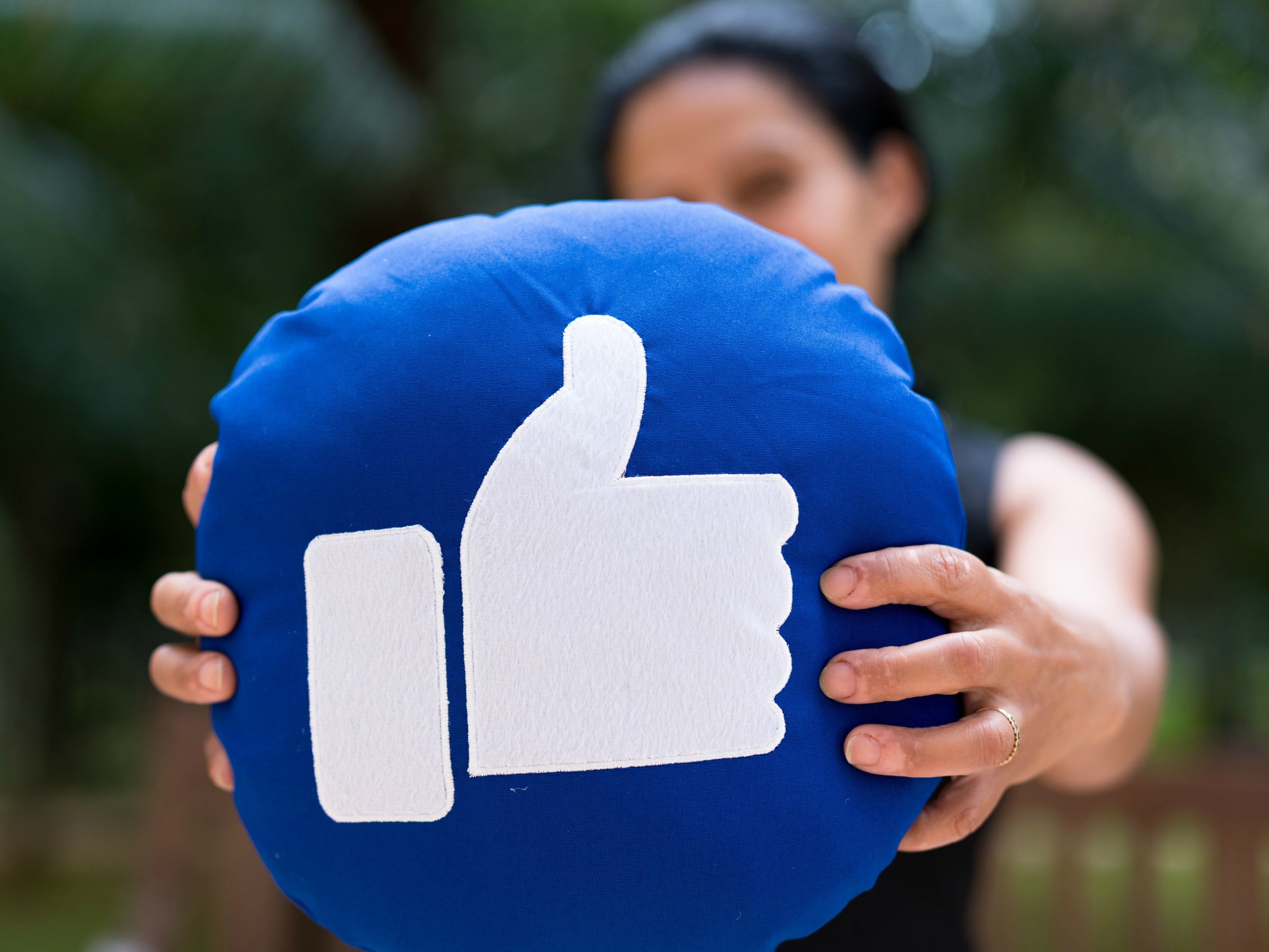 A woman holding up a pillow with the Facebook "like" icon on it.